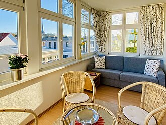Wintergarten der Ferienwohnung Villa Fortuna mit Meerblick, Schlafcouch, Glastisch und Korbstühlen