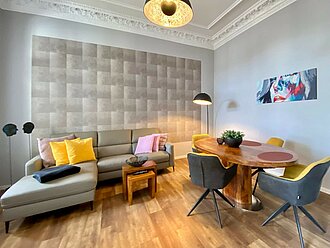 Extravagante Ferienwohnung in der Villa Anna: Historische Architektur trifft auf moderne Einrichtung: Ledercouch und Holztisch unten, weißer Stuck an der Decke.