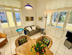 Lichtdurchfluteter Wohnbereich der weißen  Ferienwohnung 5 der Villa Caprivi mit hölzernem Esstisch und Lederzweisitzer.