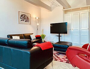 Beliebte Ferienwohnung 11 Villa Caprivi mit modernen schwarzen Ledercouchen und rotem Ledersessel auf rot gemustertem Wollteppich, Glastisch in der Mitte- komfortabel und gemütlich.