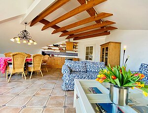 Großer Wohnraum der Ferienwohnung 12 Villa Caprivi mit Holzbalkendecke, zwei blau-weißen Sofas, Esstisch und moderner Küchenzeile.
